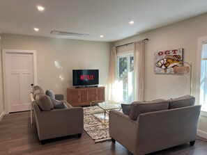 A living room with a flat-screen TV on a wooden cabinet, two grey sofas, a patterned rug, and a wall with a fish painting. - The Land and Sea at Cape Neddick / A modern 1-bedroom apartment with AC (York)