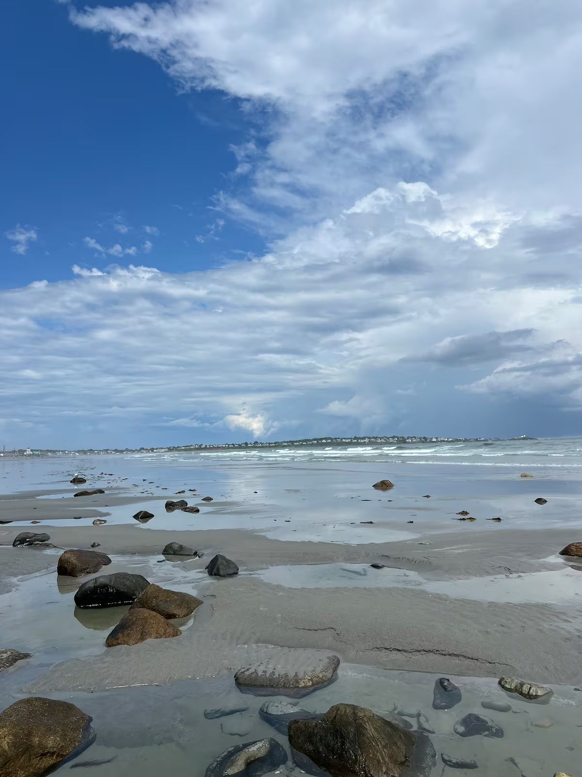 A beach with scattered rocks and calm water under a partly cloudy sky.