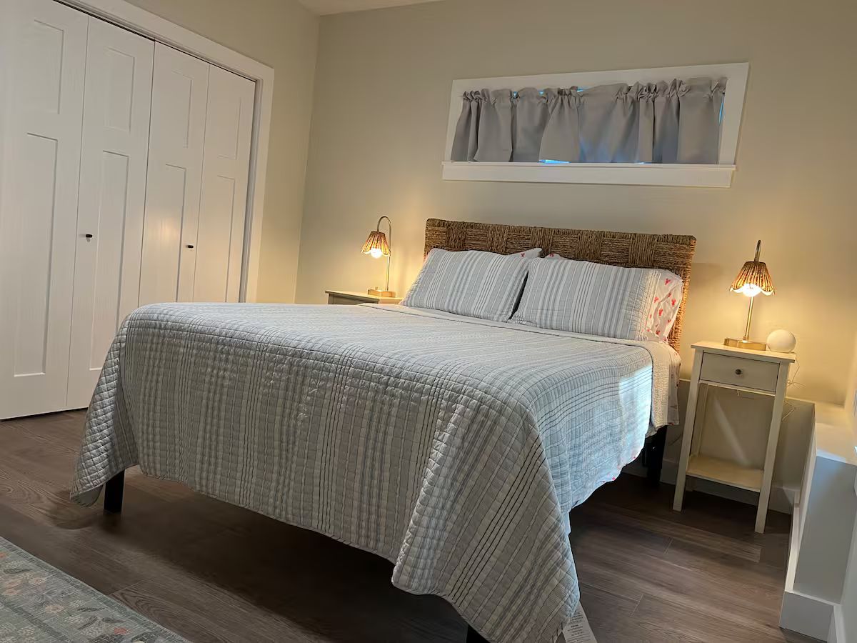 A bedroom with a bed, two bedside tables, a nightstand, a window with curtains, and a door.