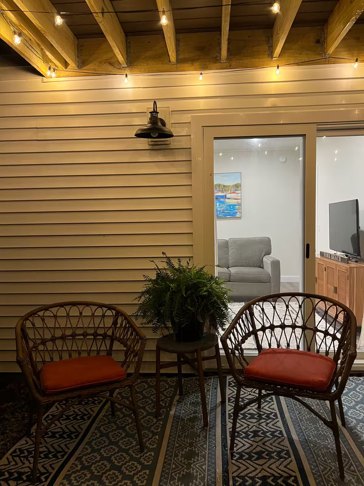 A room with two wicker chairs, a small table with a plant, and a patterned rug.