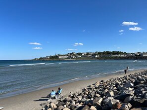 A beach with a rocky shoreline, calm sea, and houses in the background. - The Land and Sea at Cape Neddick / A modern 1-bedroom apartment with AC (York)