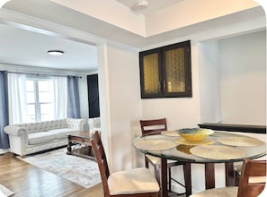 A dining area with a glass table, wooden chairs, and a white sofa in the background.