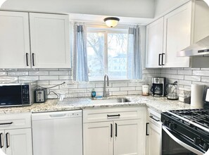 Une cuisine avec des meubles blancs, un four à micro-ondes, un grille-pain, un évier et une cuisinière.