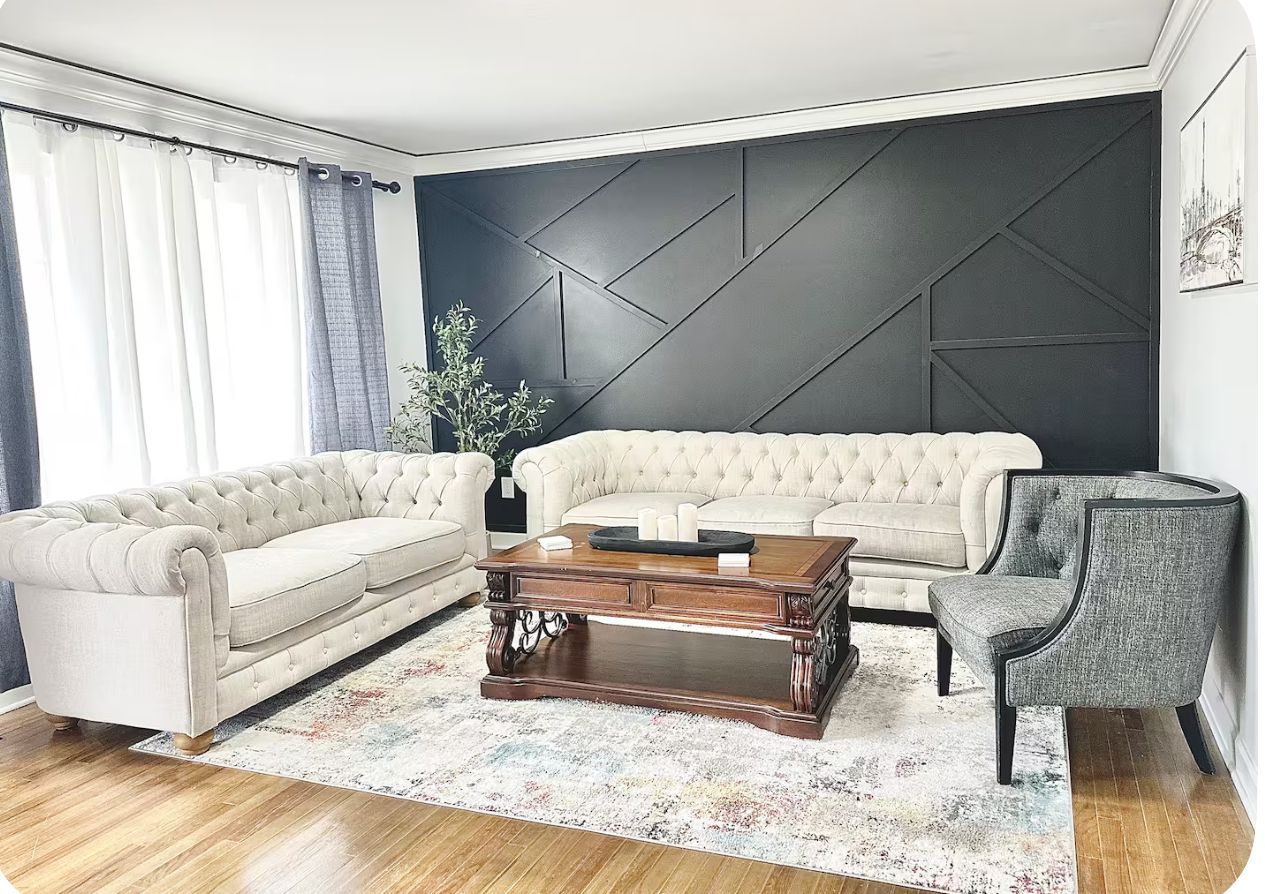 Uma sala de estar com sofá estofado, mesa de centro em madeira escura e poltrona cinza.