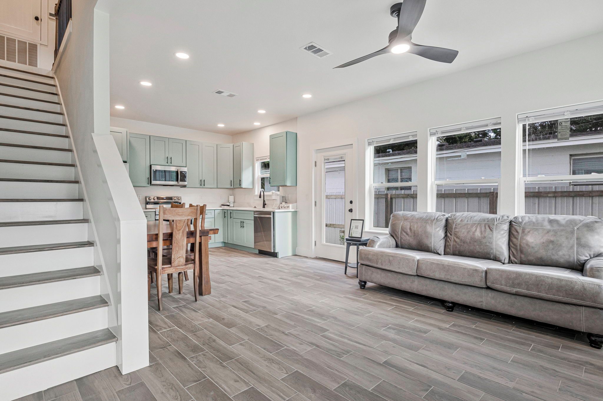 A modern kitchen with a dining area, a staircase, and a living room with a sofa.