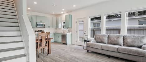 A modern kitchen with a dining area, a staircase, and a living room with a sofa.