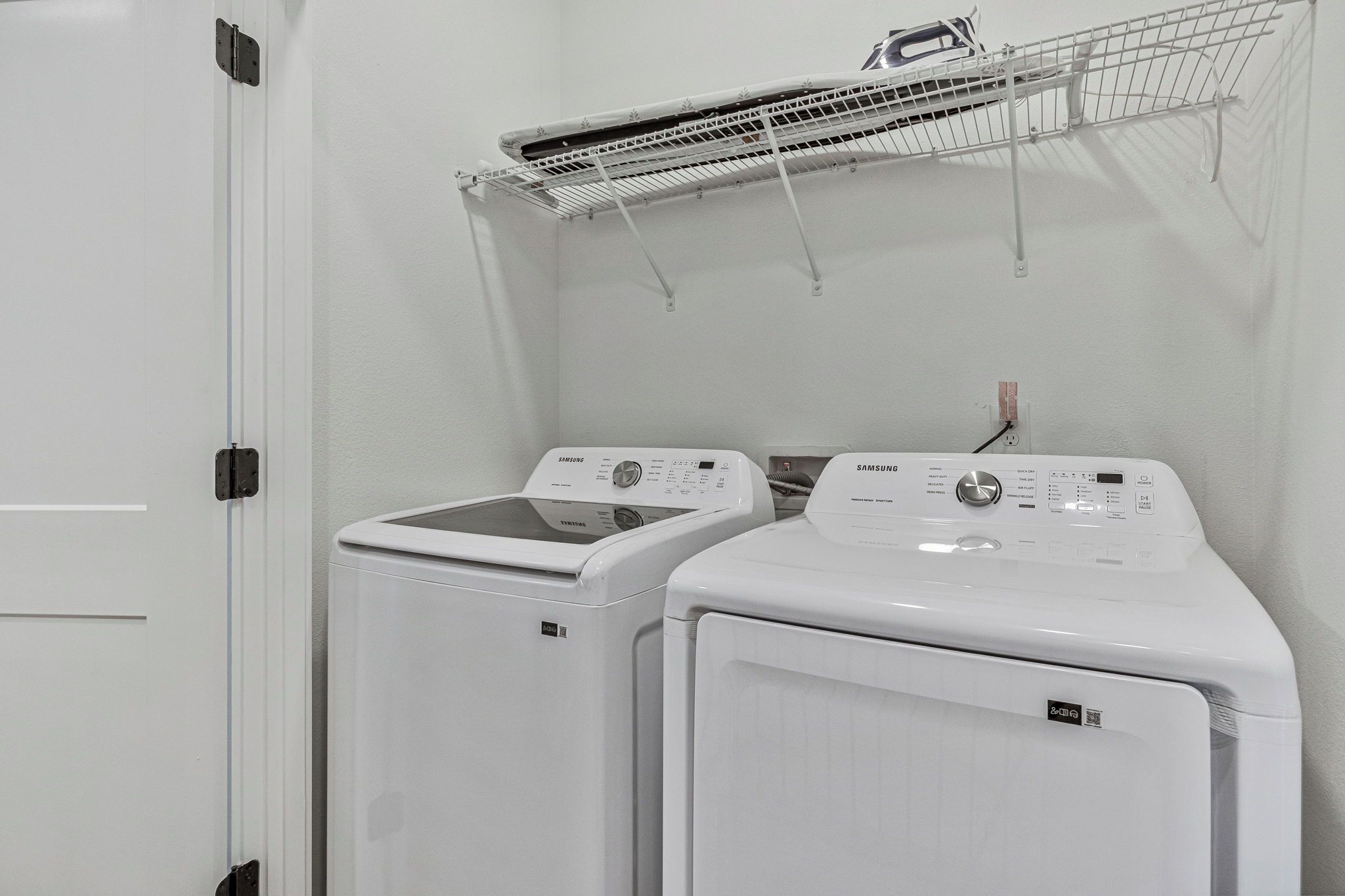 A laundry room with two front-loading washing machines and a drying rack above.