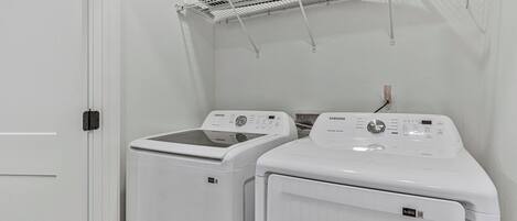 A laundry room with two front-loading washing machines and a drying rack above.