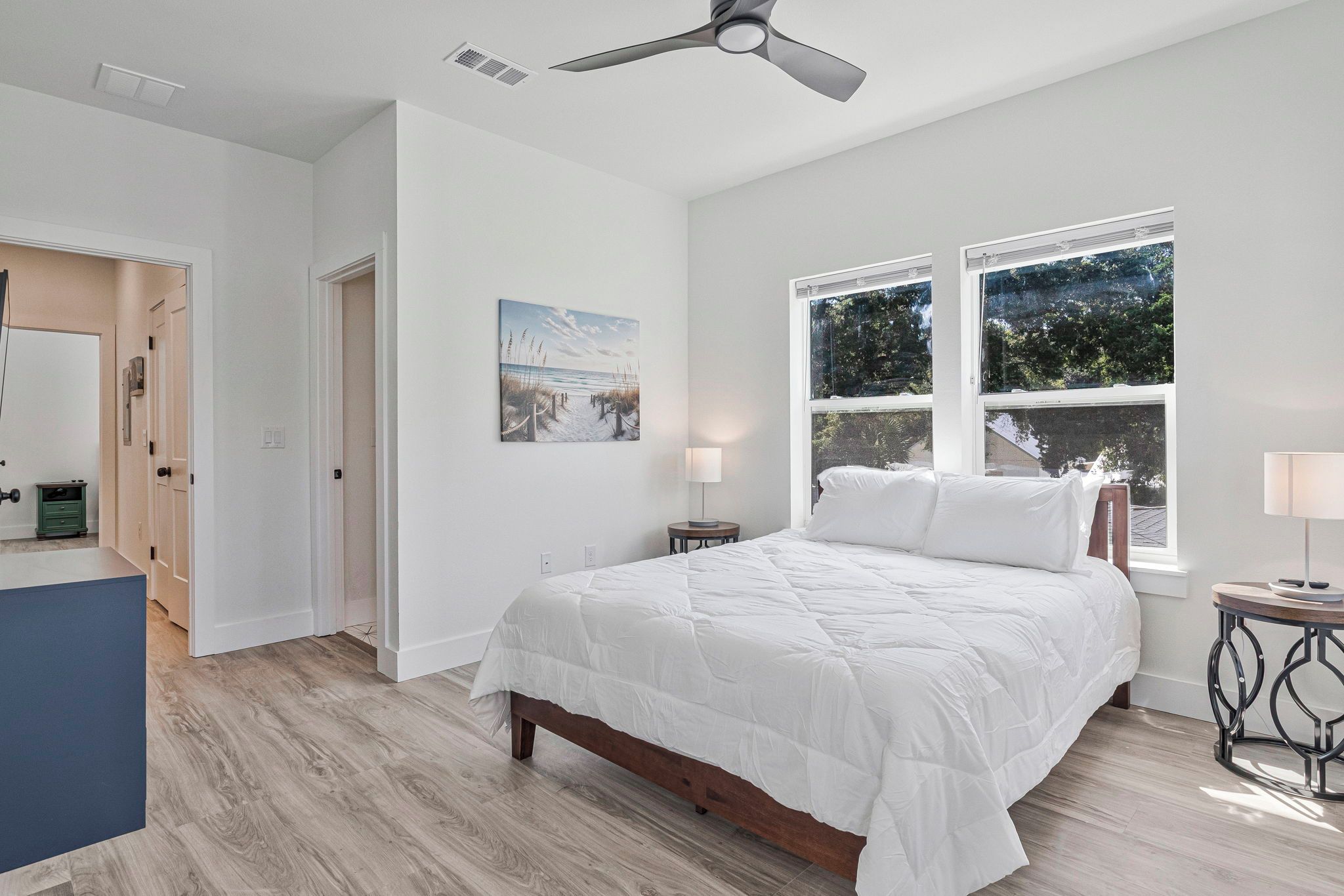 A bedroom with a bed, a ceiling fan, a window with a view, and a door.