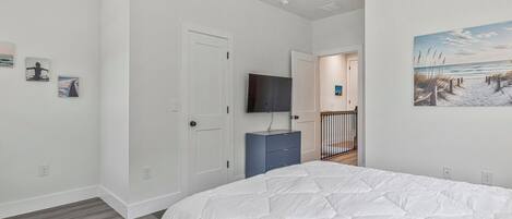 Une chambre à coucher avec un lit, un téléviseur posé sur un meuble, une porte et un couloir menant à une autre pièce.