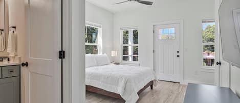 A bedroom with a bed, a ceiling fan, and a door with a window.