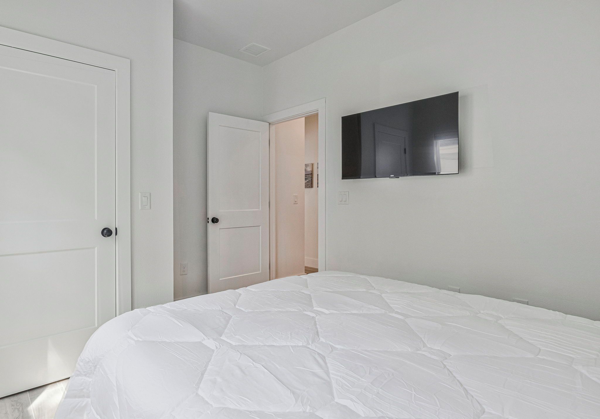 Une chambre avec un lit blanc, une porte et un téléviseur fixé au mur.