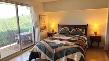 A bedroom with a large bed, two bedside lamps, a ceiling fan, a view of greenery outside, and a framed picture on the wall.