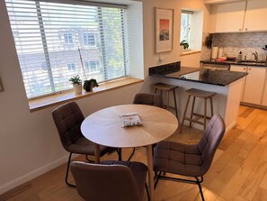 Eine moderne Küche mit Essbereich, ausgestattet mit einem runden Tisch, Barhocker und einem Fenster mit Jalousien.