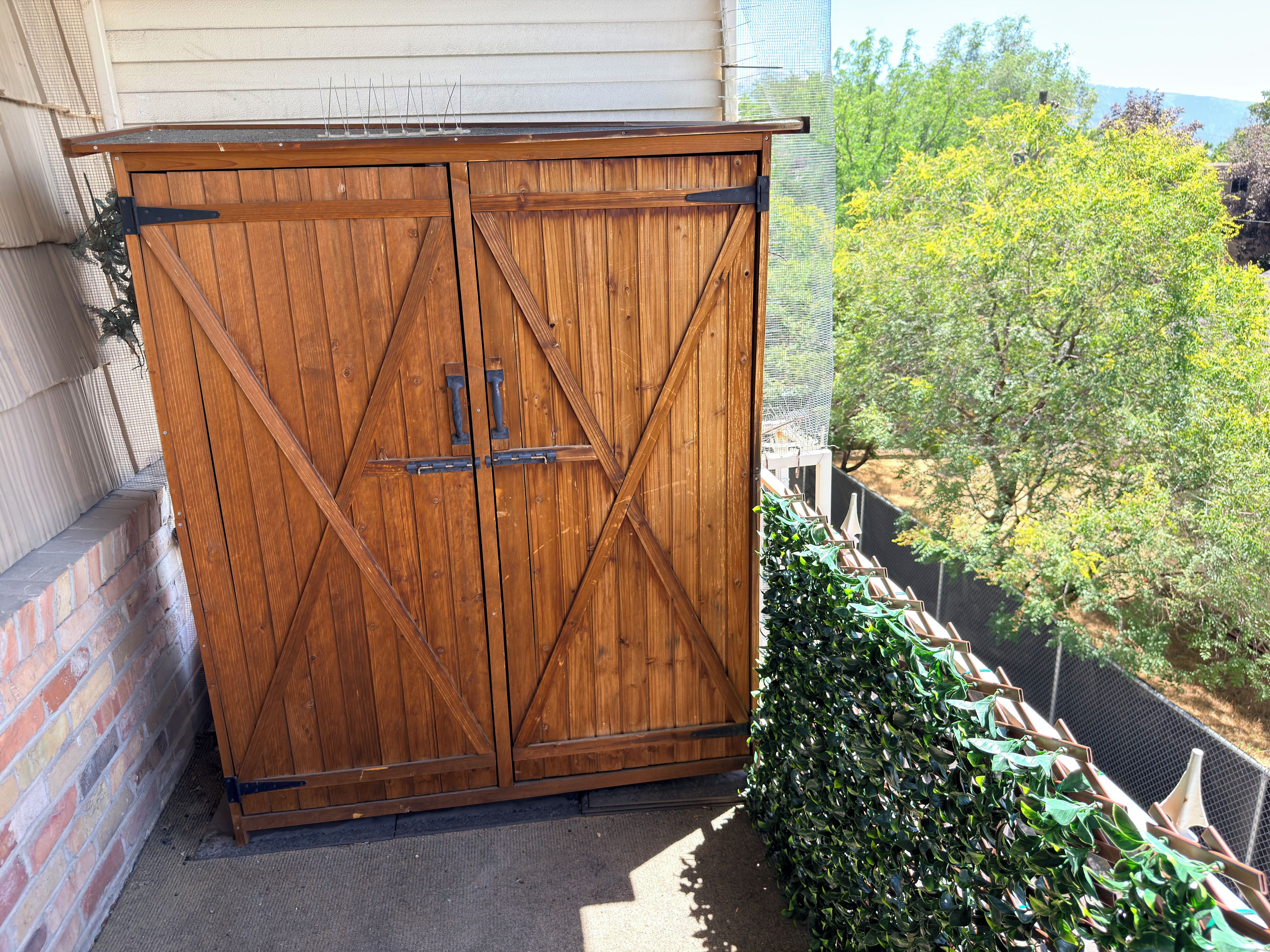 A wooden double door with metal hinges and a latch, positioned against a brick wall with a metal mesh screen.