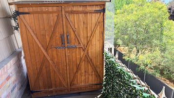 A wooden double door with metal hinges and a latch, positioned against a brick wall with a metal mesh screen.