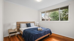 A bedroom with a bed, two bedside tables, a window, and a view of greenery outside. - Church Street Retreat (Cowes)