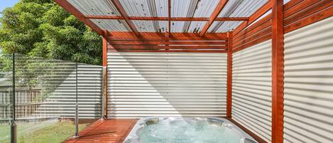 A hot tub under a wooden pergola with a corrugated metal roof.