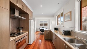 A modern kitchen with wooden cabinets, a stainless steel sink, and a dining area with a table and chairs. - Church Street Retreat (Cowes)