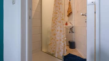A bathroom with a shower, a towel rack, a sink, and a trash bin.