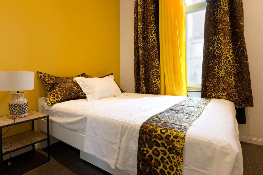 Une chambre d’hôtel avec un lit, une table de chevet, une lampe et des rideaux.
