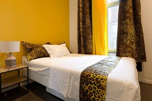 A hotel room with a bed, a nightstand, a lamp, and curtains.