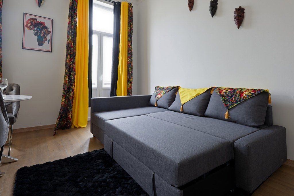 Een moderne woonkamer met een grijze bank, een zwart tapijt en een klein tafeltje met een stoel.