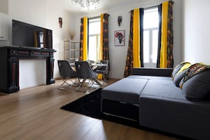 A modern living room with a sofa, a TV, a dining area, and a fireplace. - Chic and elegant 3-bedroom apartment (Molenbeek-Saint-Jean)