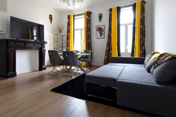 A modern living room with a sofa, a TV, a dining area, and a fireplace.