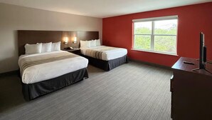 Ein Hotelzimmer mit zwei Betten, einem Schreibtisch, einem Stuhl, einem Nachttisch und einem Fenster mit Blick.