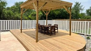 Eine Holzterrasse mit einer Pergola und einem Tisch und Stühlen darunter.