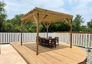 Eine Holzterrasse mit einer Pergola und einem Tisch und Stühlen darunter.
