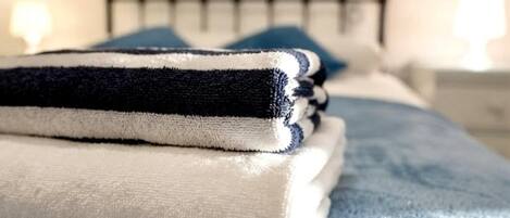 A neatly made bed with a blue blanket and a folded white and black towel on top.