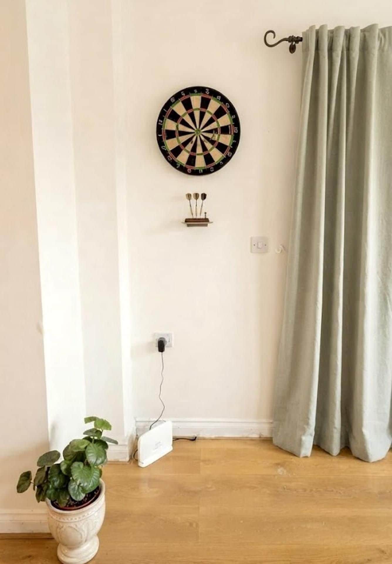 Una habitación con dardos, un enchufe, una planta en maceta y una cortina.