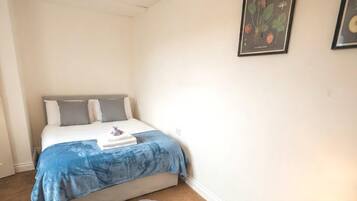 Un dormitorio con una cama, una mesita de noche con lámpara, un tapete pequeño e ilustración botánica enmarcada en la pared.