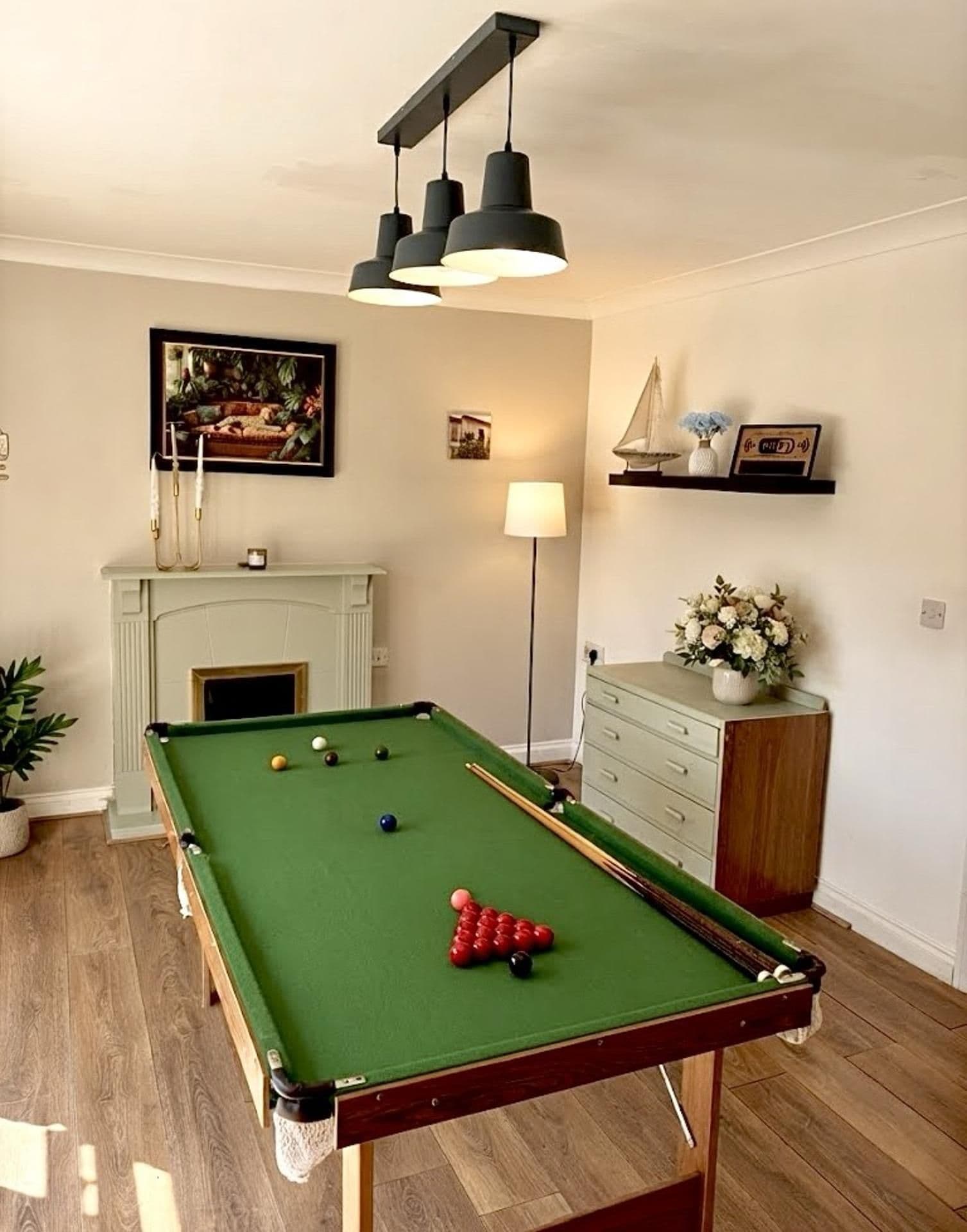 Una mesa de billar con bolas, una chimenea, una lámpara y una estantería con objetos decorativos.