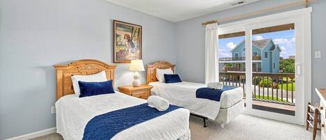 A bedroom with two beds, a nightstand, a lamp, a painting, and a sliding glass door leading to a balcony.