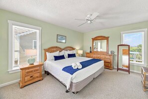 Ein Schlafzimmer mit einem Bett, Nachttischen, einem Schminktisch, einem Spiegel und einem Deckenventilator.