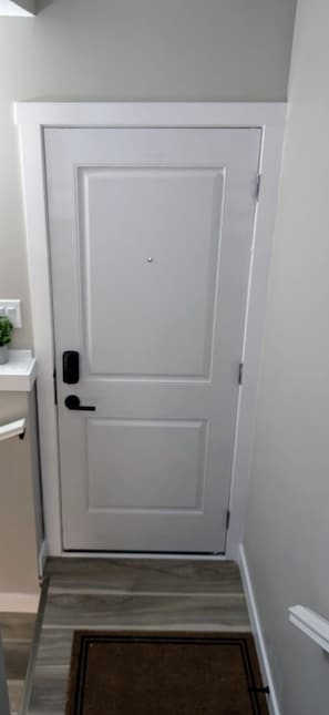Una porta blanca amb una clau i un pom, una petita planta en test amb una prestatgeria blanca, i un felp de porta marró sobre un terra de fusta.