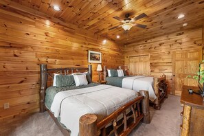 Ein schlicht eingerichtetes Schlafzimmer im Chalet-Stil mit zwei Betten, Holzwänden, einem Deckenventilator und einem gerahmten Bild an der Wand.