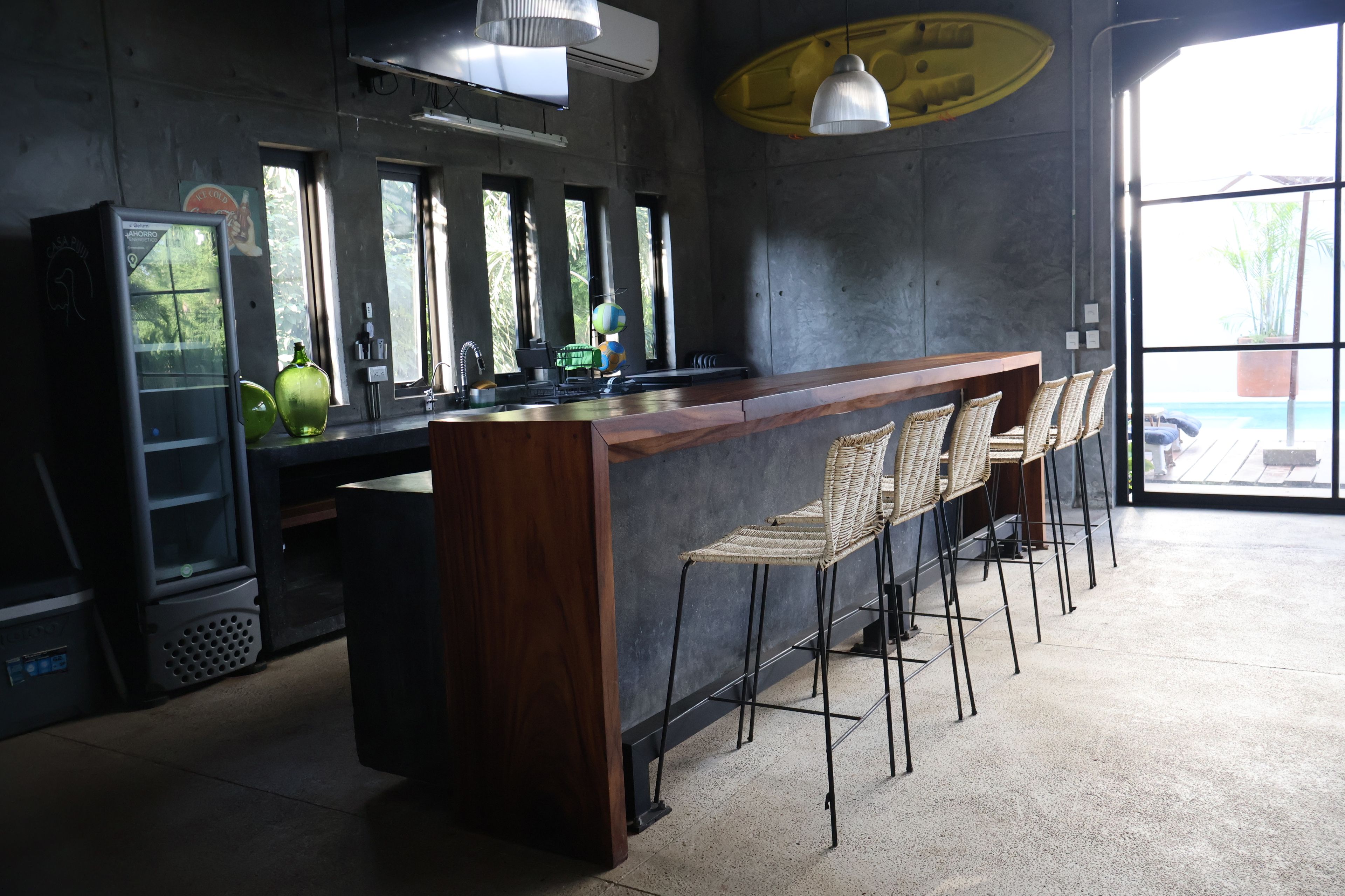 A bar area with a wooden counter, bar stools, and a large window providing a view outside.