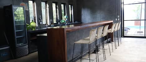 A bar area with a wooden counter, bar stools, and a large window providing a view outside.