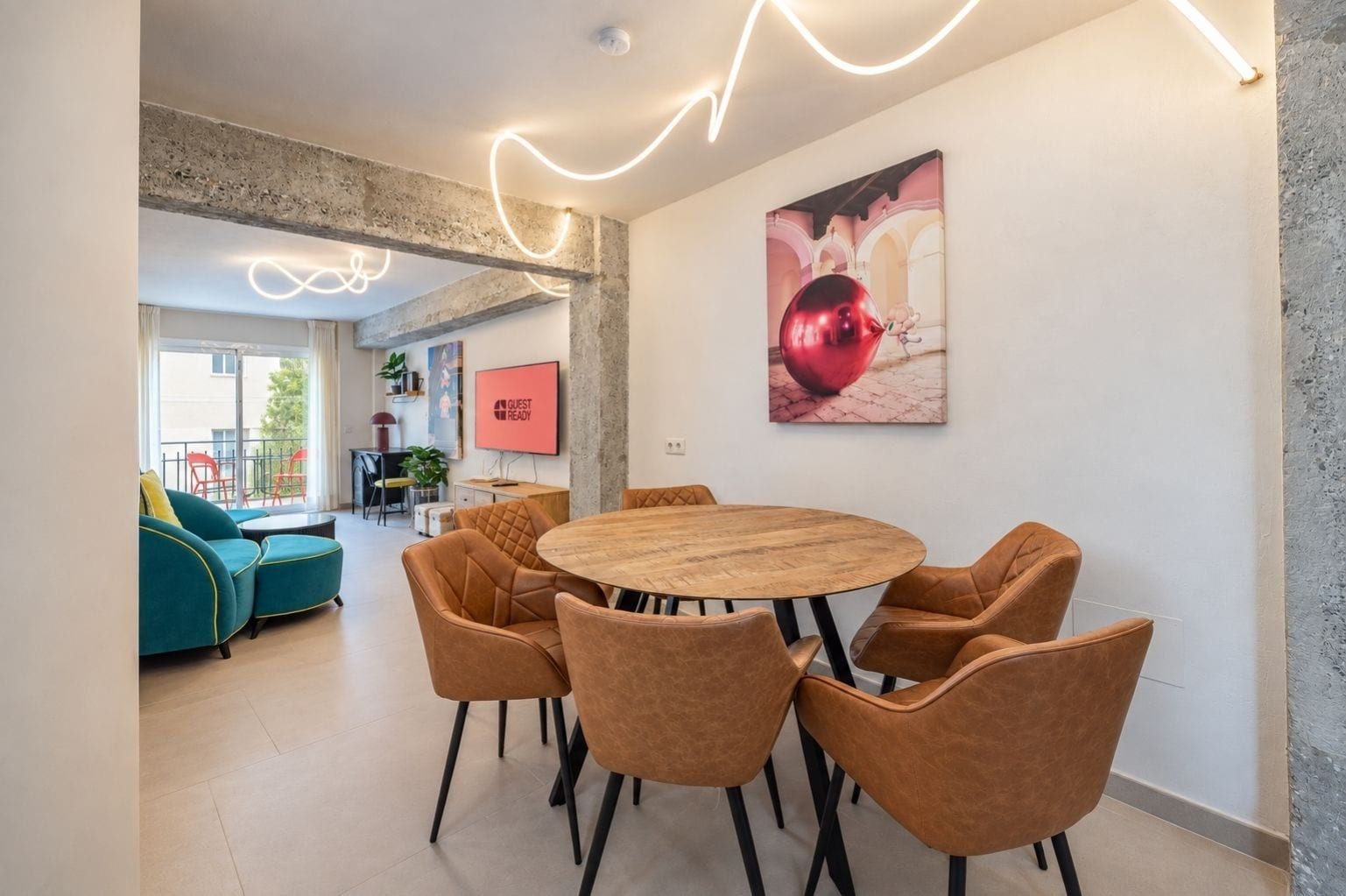 Ein modernes Interieur mit einem runden Holztisch, der von Ledersesseln umgeben ist, einem großen, an der Wand befestigten Fernseher und einem gerahmten Kunstwerk.