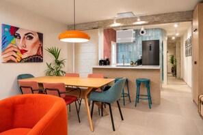 A modern kitchen with a central island, a dining area with colorful chairs, and a large painting on the wall. - Guestready - Malaga Art and Comfort Apartments (Málaga)