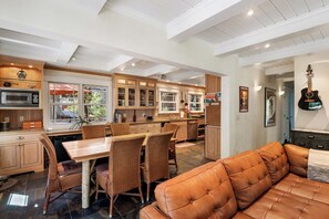 A spacious kitchen with wooden cabinets, a dining area with wicker chairs, and a leather sofa. - Kimberly Luxury Cabin - Hot Tub, Walk to Town (Tahoe City)