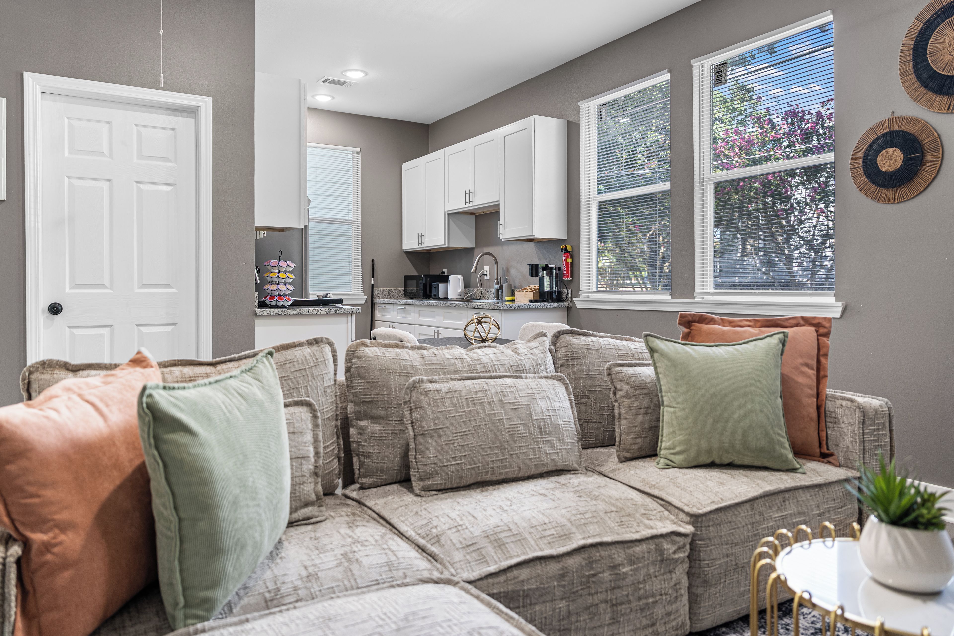 A living room with a sectional sofa, a dining table with chairs, and a kitchen area with cabinets and appliances.