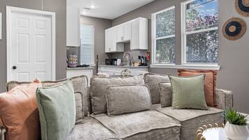 A living room with a sectional sofa, a dining table with chairs, and a kitchen area with cabinets and appliances.