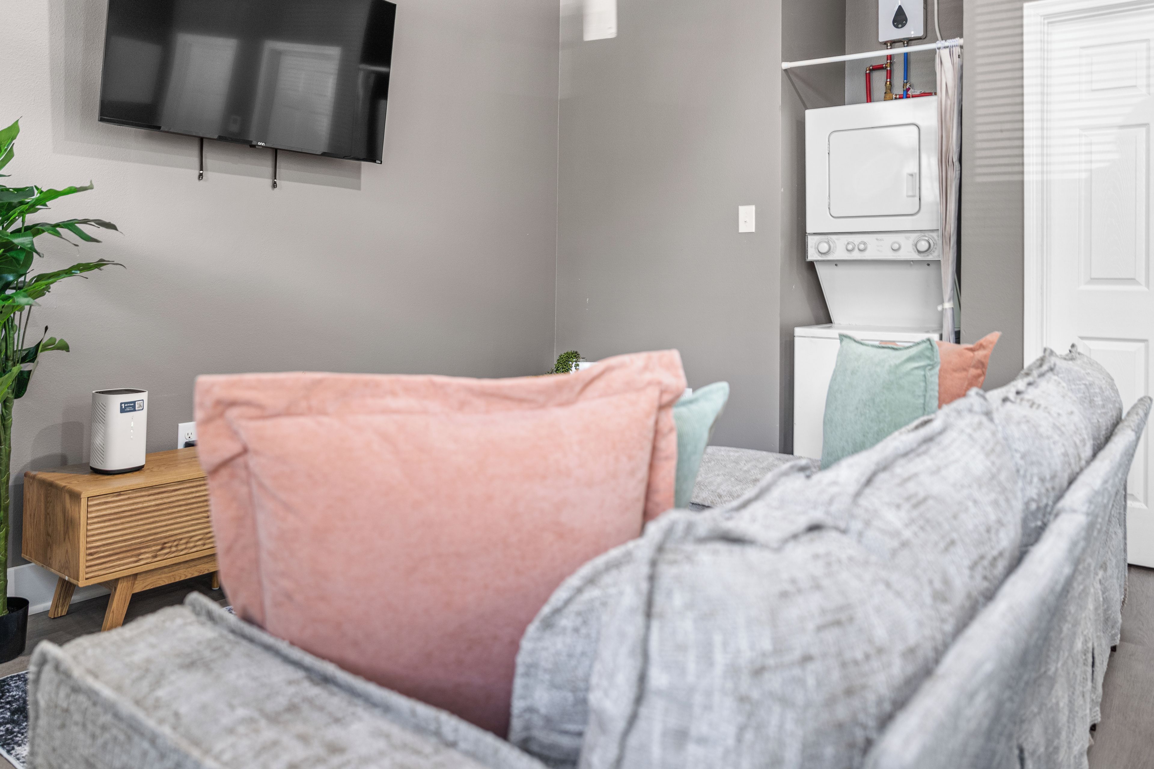 Ein modernes Schlafzimmer mit Bett, einem an der Wand befestigten Fernseher, einer Waschmaschine und einer Pflanze.