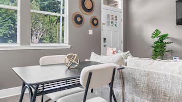 Ein Zimmer mit Esstisch, Stühlen, einer Couch, einer Zimmerpflanze und Wanddekorationen.