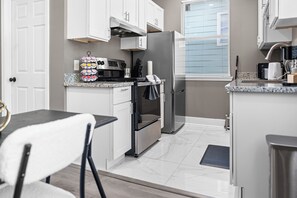 Eine moderne Küche mit weißen Schränken, einem Edelstahlkühlschrank und einer Essecke mit einem schwarzen Stuhl.
